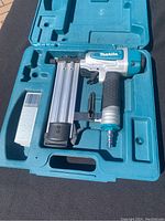 Makita pneumatic brad nailer in blue plastic carrying case with brad nail strips beside it.