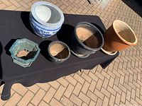 Five assorted garden pots displayed on black cloth outdoors on brick ground.