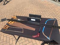 Five saws displayed on a black tablecloth with two rectangular black plastic boxes and a straight edge placed.