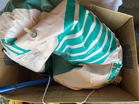 Inflatable boat partially inflated showing green and white stripes, deflation valve, and blue paddle in box