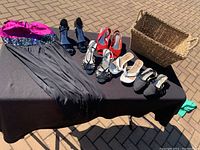 All items on black cloth on outdoor floor showing dress, four pairs of high-heeled shoes, and basket.