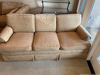 Front angled view of beige three cushion couch showing seat cushions, back cushions, armrests and skirted base.
