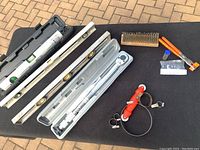 Three bubble levels, laser level in carrying case, torque wrench case, hand tools including wire brush, hose clamps and bolt cutters arranged on table.