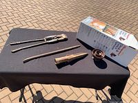 Overview of the four items including the bolt cutters, prying tool, mallet, and boxed garden sprayer displayed on a black cloth against a paved background.
