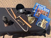 Overview of tools and home repair books including hammers, crowbar, jack, pipe wrench, funnels, and home repair books on black tablecloth.