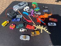 Photo showing assortment of small toy vehicles including die-cast cars, toy bus, troll doll, miniature hockey sticks, plastic figurines, and a silver RC car with remote