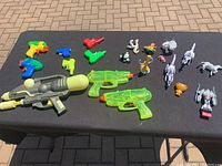 Photo showing small colorful plastic water shooters and some toy animal and character figurines arranged on a black surface.