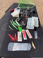 Full view of fishing lures, metal rod holders, tackle boxes, downrigger weight plate, and assorted hooks and wires laid out on black cloth.