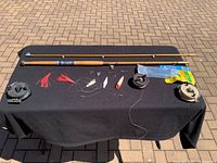 Top view of fishing rod, reels, lures, and flasher on black cloth