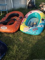 Photo of two inflatable boats on the grass, one orange with black accents, the other multi-colored, both with '200' labels visible.