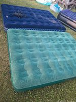 Two double-sized flocked inflatable mattresses, one dark blue and one green, displayed outdoors on grass.