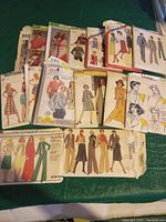 Photo showing assorted vintage and antique sewing patterns spread out, including Butterick, Vogue, and others with illustrations of dresses, skirts, and jackets.
