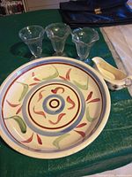 Top view of large decorative bowl with colorful pattern along with three glass sundae cups and a ceramic gravy boat on a green table.