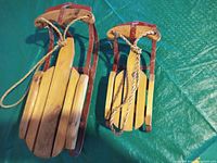 Two antique wooden sleds of different sizes shown on a green tarp surface.