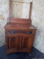 Antique wooden washstand showing drawer, cabinet doors, mirror frame, and top surface with water stains.