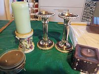 Set of two chrome pedestal candle holders with crystal-like stones on bases, next to various candles on green table.