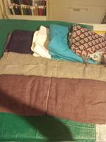 Photo showing multiple folded fabric pieces in various colors including purple, cream, teal, light brown, maroon, and a burgundy/pink patterned fabric.