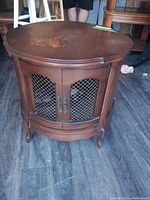 Front view of a wooden drum table with visible surface damage on the top, metal mesh cabinet doors, and curved legs.