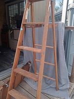 Photo of wooden A-frame ladder with paint stains and four wide steps, standing on a wooden deck.