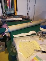 Full view of the bolt of green fabric rolled on a tube lying on a pool table with some notes on top.