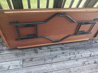 Underside of the wooden table showing black metal folding legs and support structure including hinges and mounting brackets.