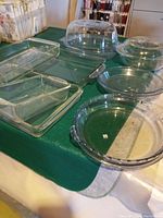 Photo of all glass baking dishes arranged on table showing variety of sizes and shapes including rectangular, round, and oval dishes, some with lids.