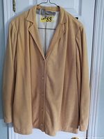 Front view of the light tan lambskin shirt jacket hanging on a hanger showing button closure and classic collar.