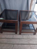 Two wood and glass end tables side by side on wooden floor, showing top and side views.