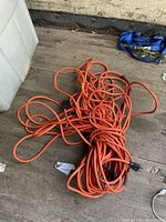 Photo of a single 50 ft orange extension cord lying on a wooden surface, showing some tape repair on part of the cord, with standard three-prong plugs on each end.