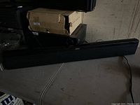 Black Bose soundbar speaker unit placed horizontally on a surface with some boxes and electronic devices in the background.