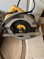 DeWalt circular saw showing yellow handle, black blade with yellow label, metal base plate, and power cord coiled on top.