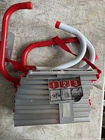 Folded aluminum ladder with red and white hooks showing usage instructions attached.