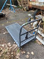 View of one dolly showing perforated metal platform and tubular handle with strap.