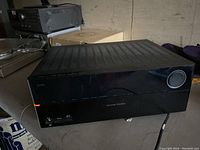 Front angled view of the Harman Kardon stereo receiver showing the power indicator light on and volume knob.