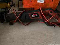 Photo shows a Jobmate reciprocating saw with black and red casing and attached red power cable. The brand label is visible on the body.