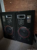 Pair of large black Samurai Model 518 speakers with red-ringed woofers, mid-range drivers, and horn tweeters, placed on a wooden floor against a wall.