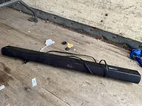 Full view of LG sound bar on a wood surface with attached power cord, shows length and shape of the device.