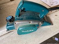 Side angle view of a blue Makita electric wood planer with visible adjustment knob and Makita logo.