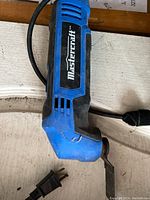 Side view of blue and black Mastercraft reciprocating tool with power cord and blade attachment on a wooden surface.