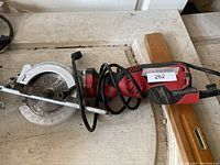 Mini circular saw with red and black handle and metal blade guard on a work surface with a power cord coiled over it.
