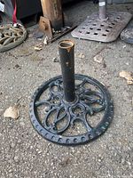 Photo of black metal patio umbrella holder on ground showing decorative open scrollwork base and rust spots