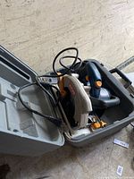 Ryobi circular saw placed inside the molded gray plastic carrying case showing the saw with black and gray body, orange trigger and blade guard, and an attached power cord.