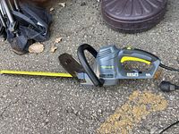 Photo showing the Yardworks electric bush trimmer laid on pavement with the power cord and the blade guard visible, highlighting the trimmer's overall condition and features.