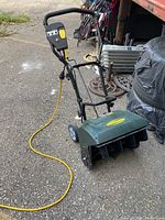 Image showing full yardworks snow thrower with black handle, green housing, yellow power switch, and yellow electrical cord on pavement.