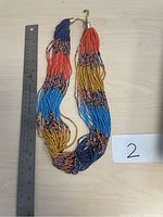 Photo of a multistrand beaded necklace with bright colors laid flat on a light surface next to a ruler for size reference.