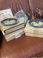 Photo showing six blue and white cameo Ulysses plates and two colorful Norman Rockwell plates, some wrapped and boxed