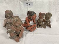 Four Mexican clay statuettes arranged on a white cloth background showcasing various poses and details