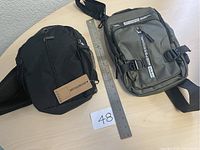 Photo showing both black and gray cross body travel bags next to a ruler for scale.