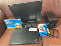 Photo of Lenovo ThinkPad laptop closed, Fujitsu monitor, HP external device, box of overlabor label sheets and accessories