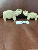 Photo showing both elephant sculptures on a brown surface, displaying size difference and material finish.